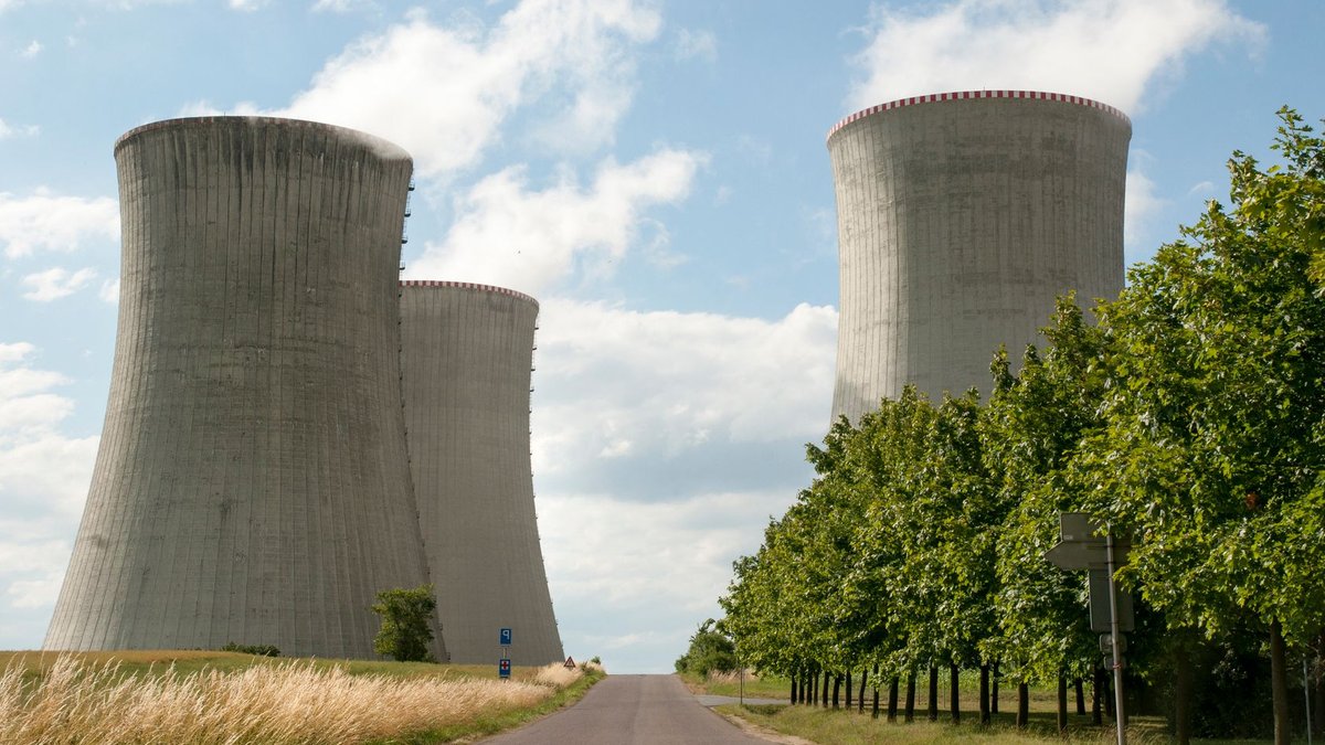 A nuclear power plant cooling towers by a road with green trees under a clear sky.