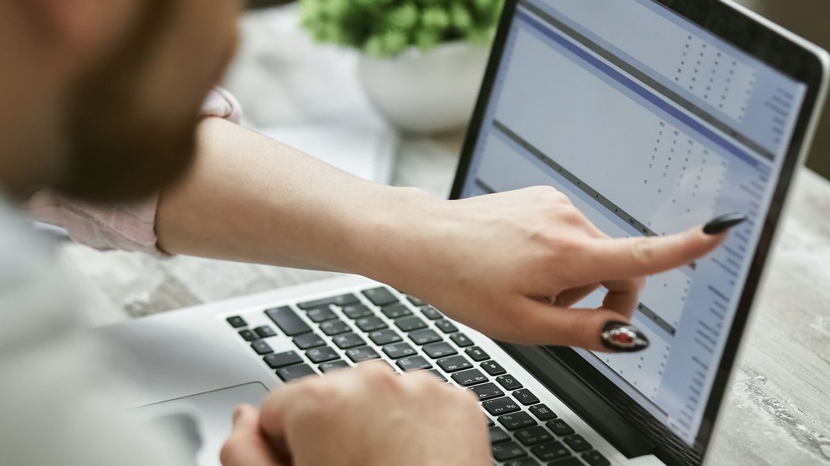 Two people working on a laptop analyzing data, pointing at screen.