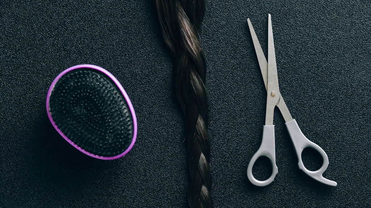 Close-up of hairdressing scissors, braided hair, and brush on black background.