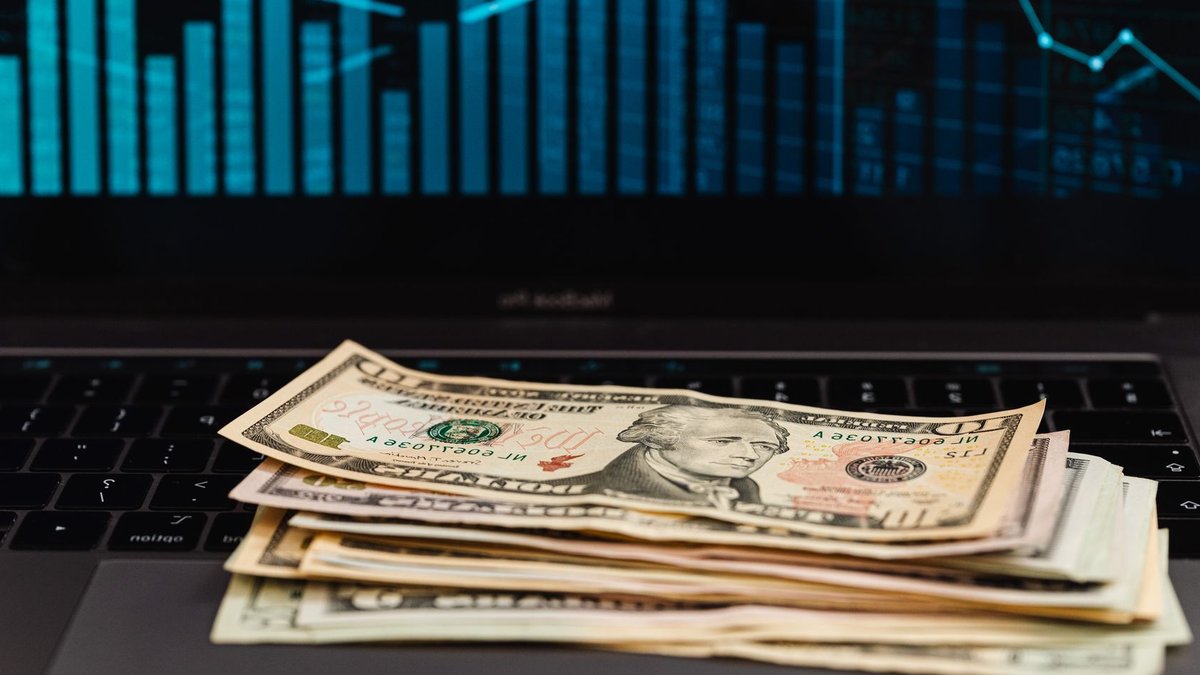 US dollar bills on laptop with financial graph in background, symbolizing wealth and technology.