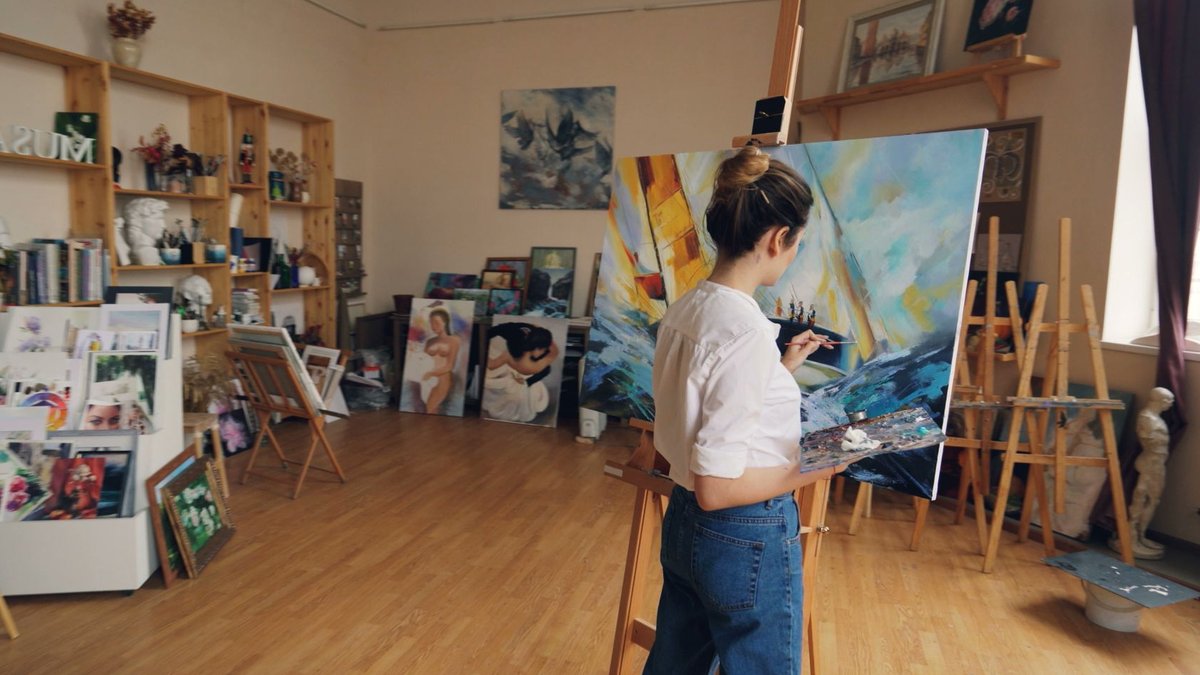 A dedicated artist working on a colorful canvas in a bright, organized studio.