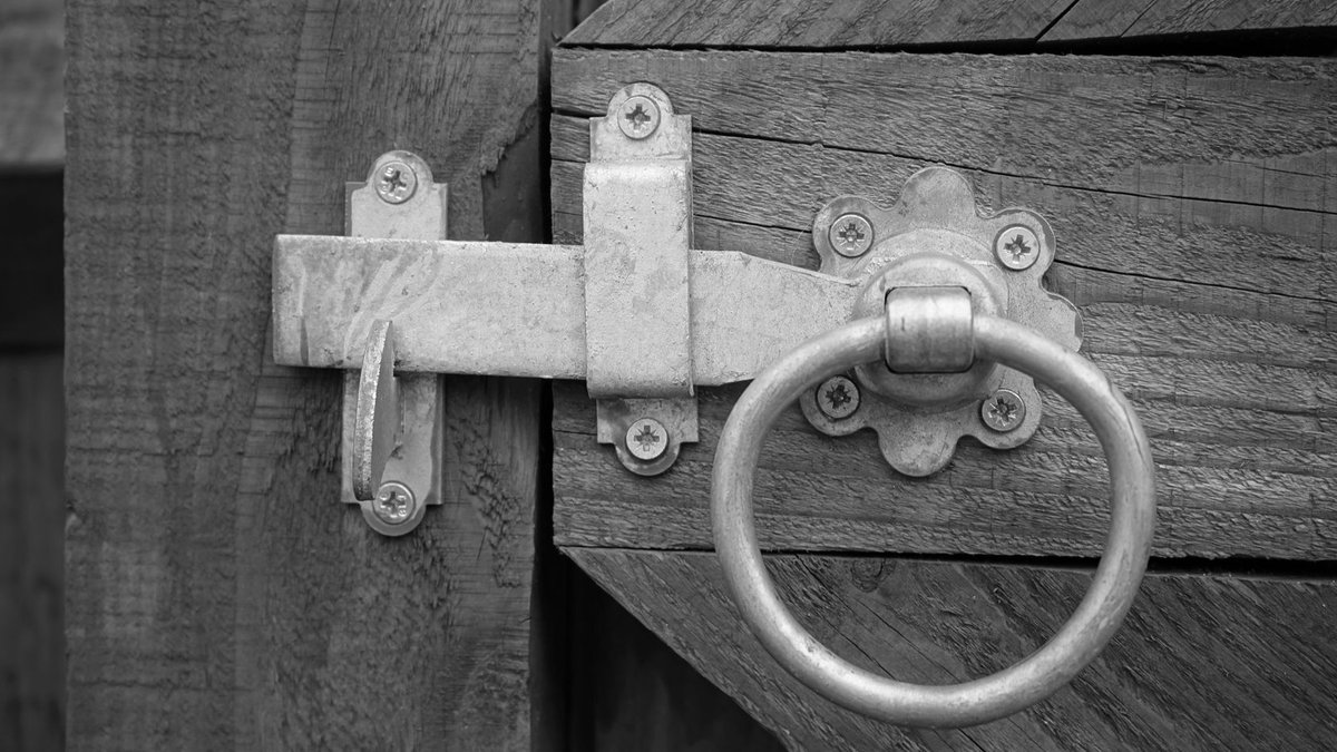 Close-up of a rustic wooden gate featuring a metal latch with a ring handle, blending vintage and security elements.