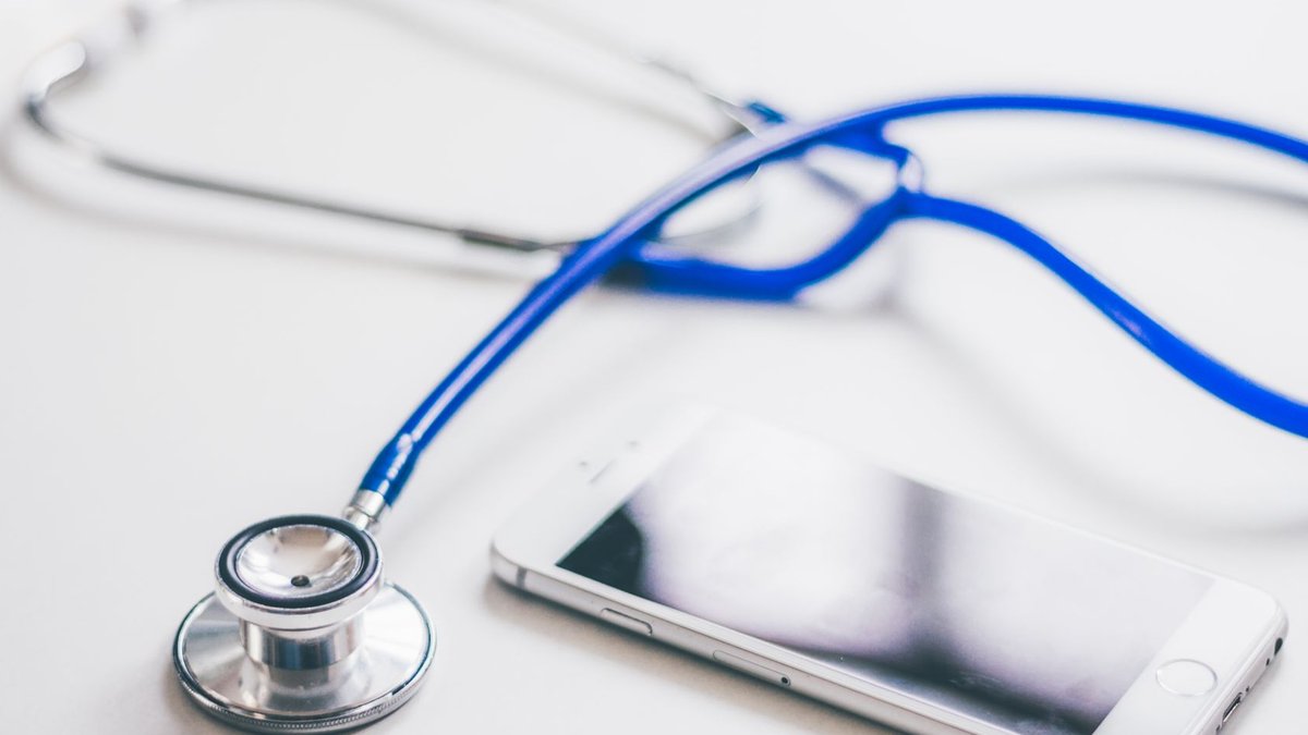 UK firms push for faster NHS access to cutting-edge drugs A smartphone and blue stethoscope on a clean white surface, emphasizing modern healthcare.
