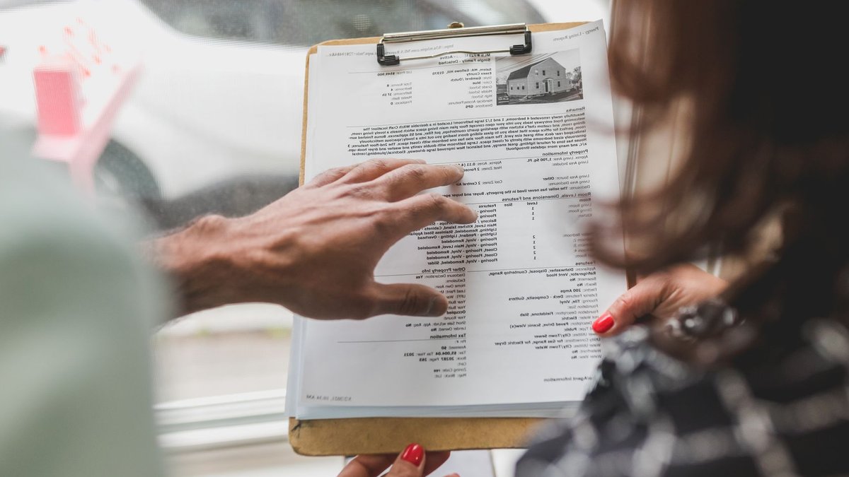 Independent real estate agents face costly tax traps Real estate agent discussing property details with client using a clipboard indoors.
