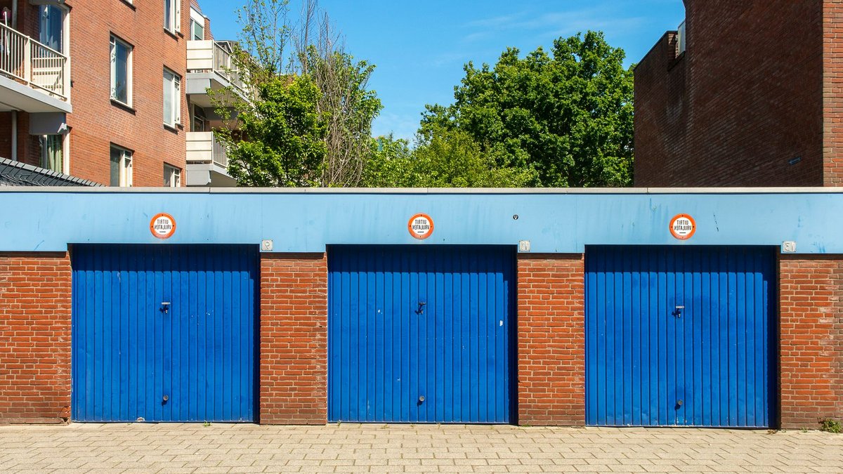 Three blue garage doors in a brick building on a sunny day.