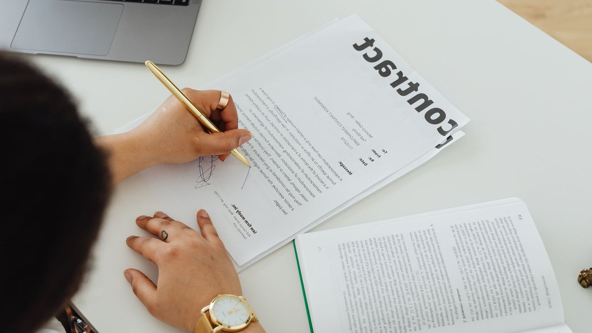Professional signing a business contract at a modern desk setup for office work.