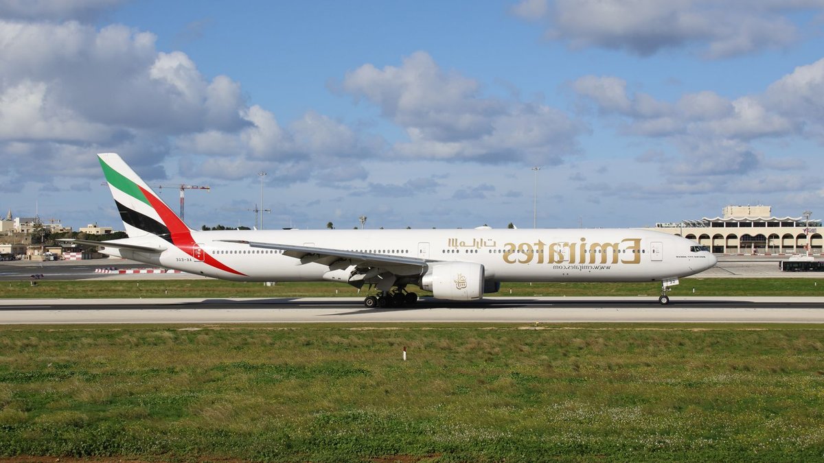 Emirates expands flights and premium services Emirates airplane parked on a sunny day at an airport runway under blue skies.