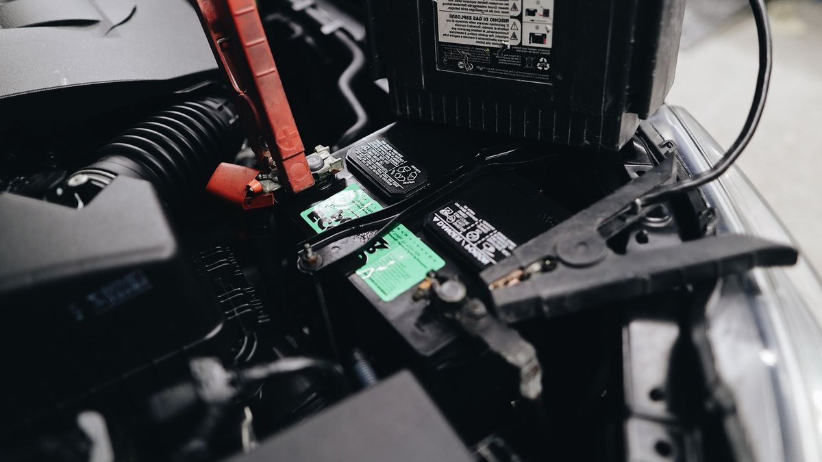 Detailed view of a car battery being jump-started with cables in an engine bay.