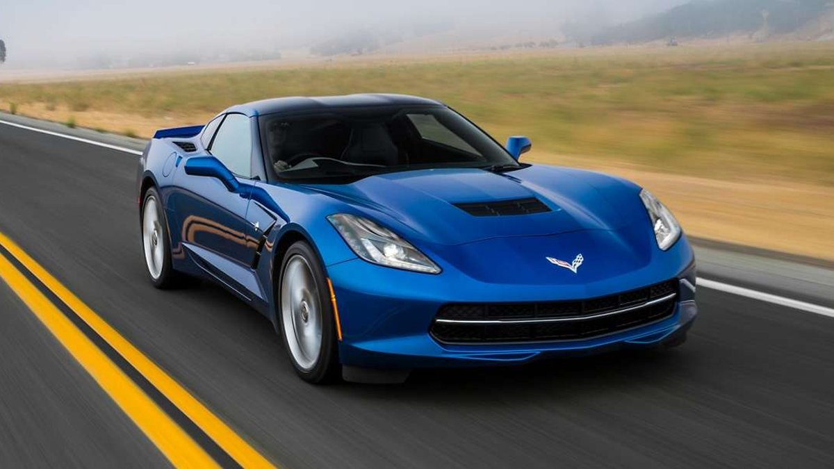 Blue 2014 Chevrolet Corvette C7 Stingray driving on a two-lane road, viewed from the front and side.