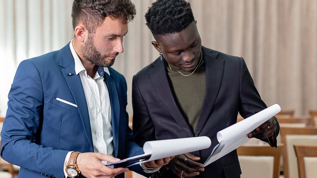 Salient targets auto lending with software solution Two businessmen in suits reviewing contracts and business documents indoors.