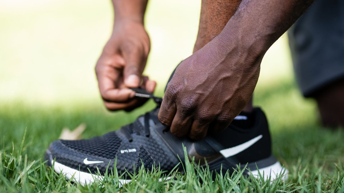 Close-up of a person tying the laces on a black running shoe on grass.