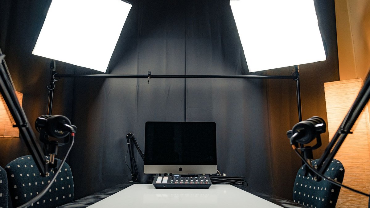 A modern podcast recording studio with microphones, lighting, and computer equipment.