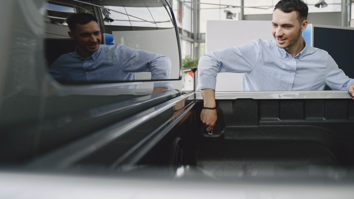 Man in a showroom examining the bed of a pickup truck, reflecting natural curiosity.