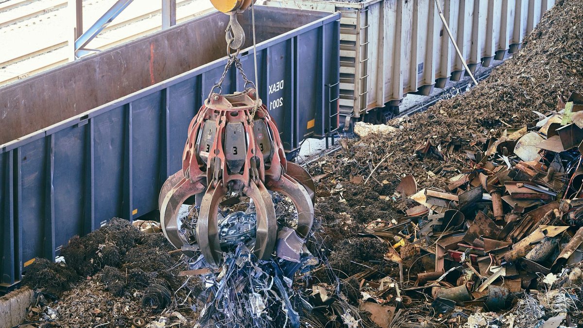 A claw crane lifting scrap metal in an industrial recycling facility.