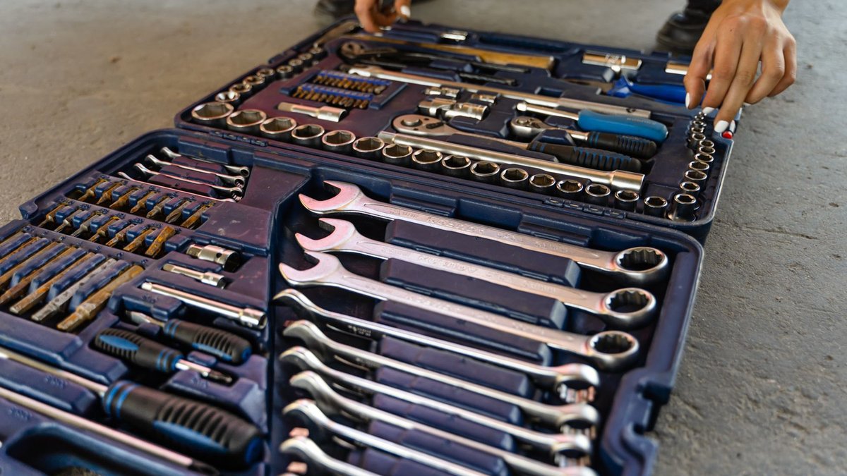 Close-up view of an open toolbox on a concrete floor, displaying various hand tools including wrenches, screwdrivers, and soc