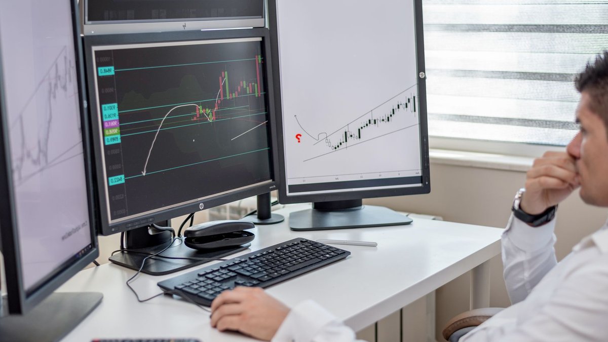 Business professional analyzing financial data on multiple computer monitors at his workspace.
