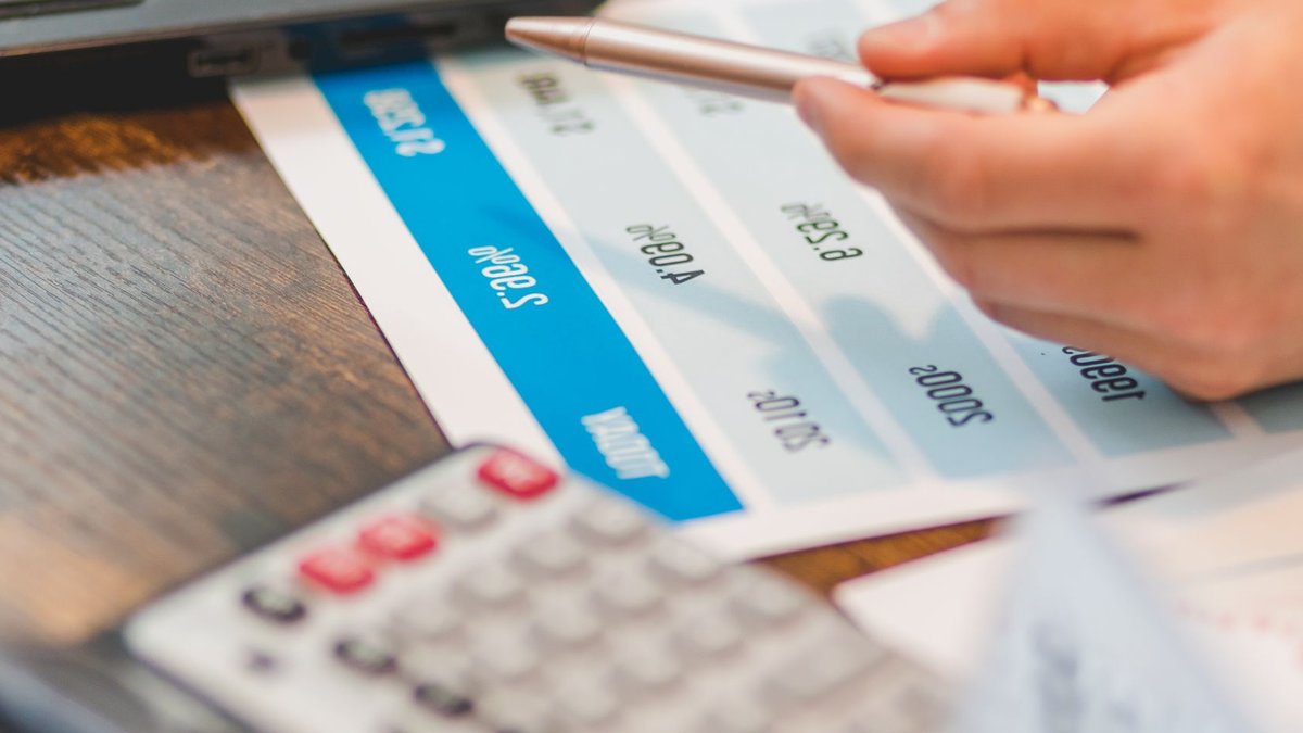 Close-up of a hand using a ballpen and calculator to analyze interest rates on a chart.