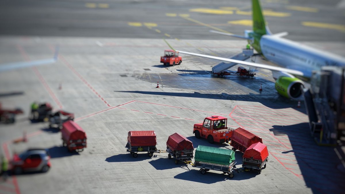 Çelebi bids for Dhaka terminal ground handling Sunlit airplane and baggage carts on airport tarmac, captured from above, showcasing transportation dynamics.