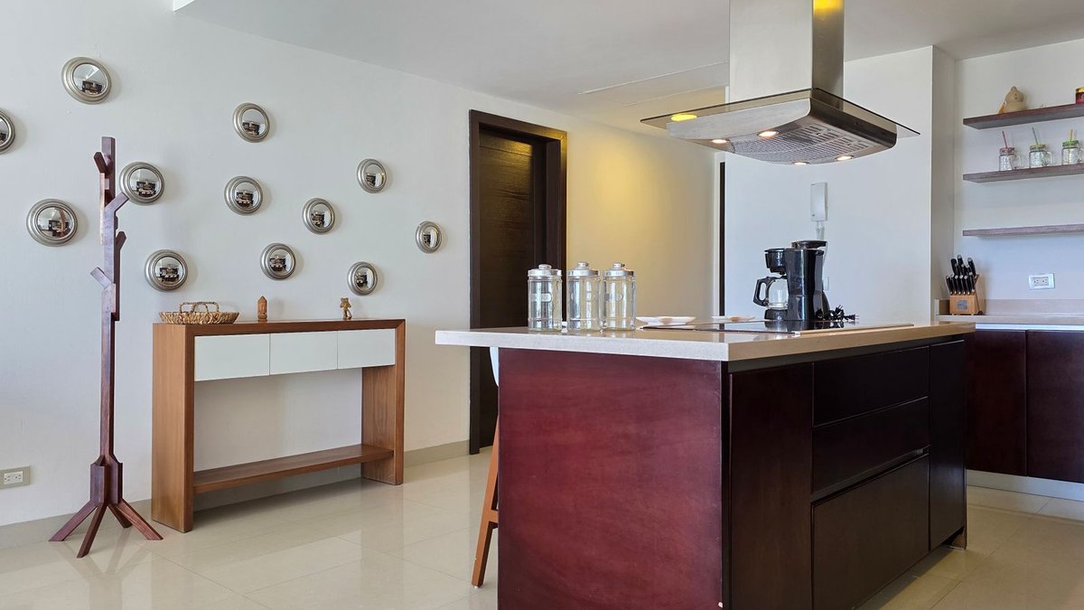 Designers Favor Semi-Enclosed Kitchens Over Open Layouts Sleek modern kitchen with central island, stainless steel decor, and wall-mounted art.