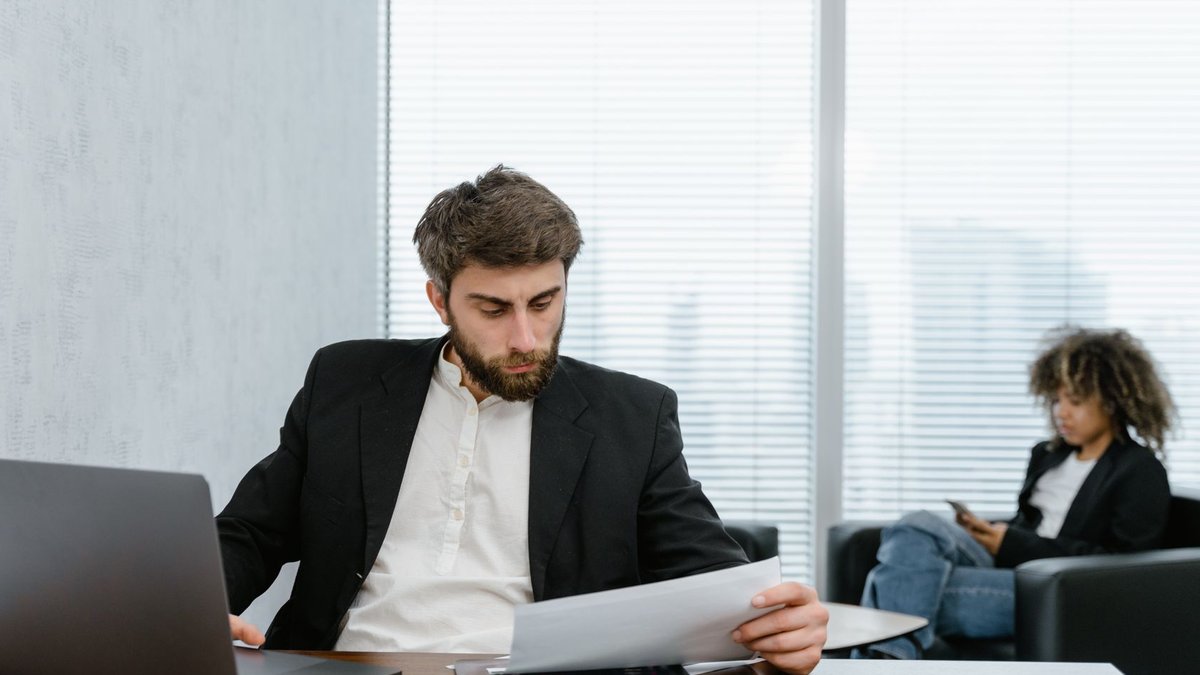Focused businessman reviews financial reports at office desk with laptop.