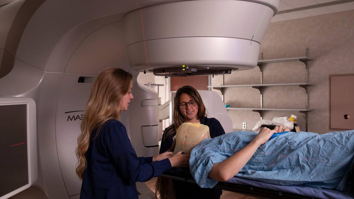 Mayo Clinic tests low-dose radiation to slow Parkinson’s progression Two radiation therapy professionals position a patient wearing a protective mesh mask beneath a linear accelerator for treatm