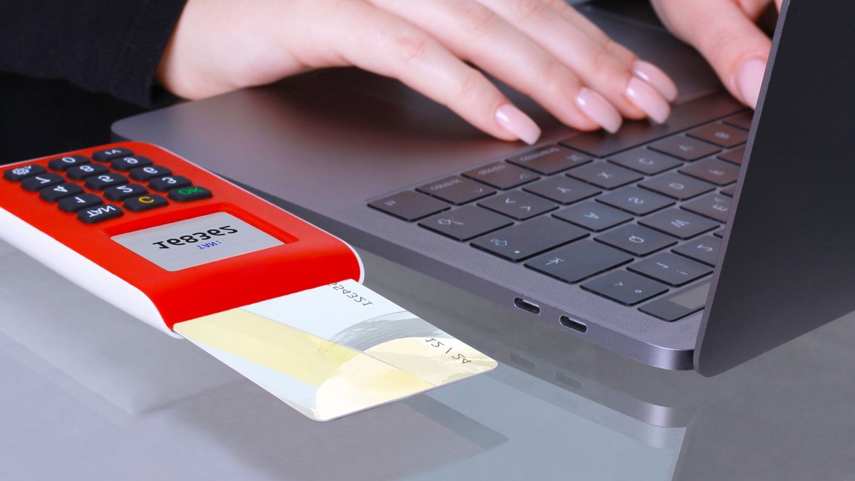 Close-up of hands using laptop and card reader for online payment.