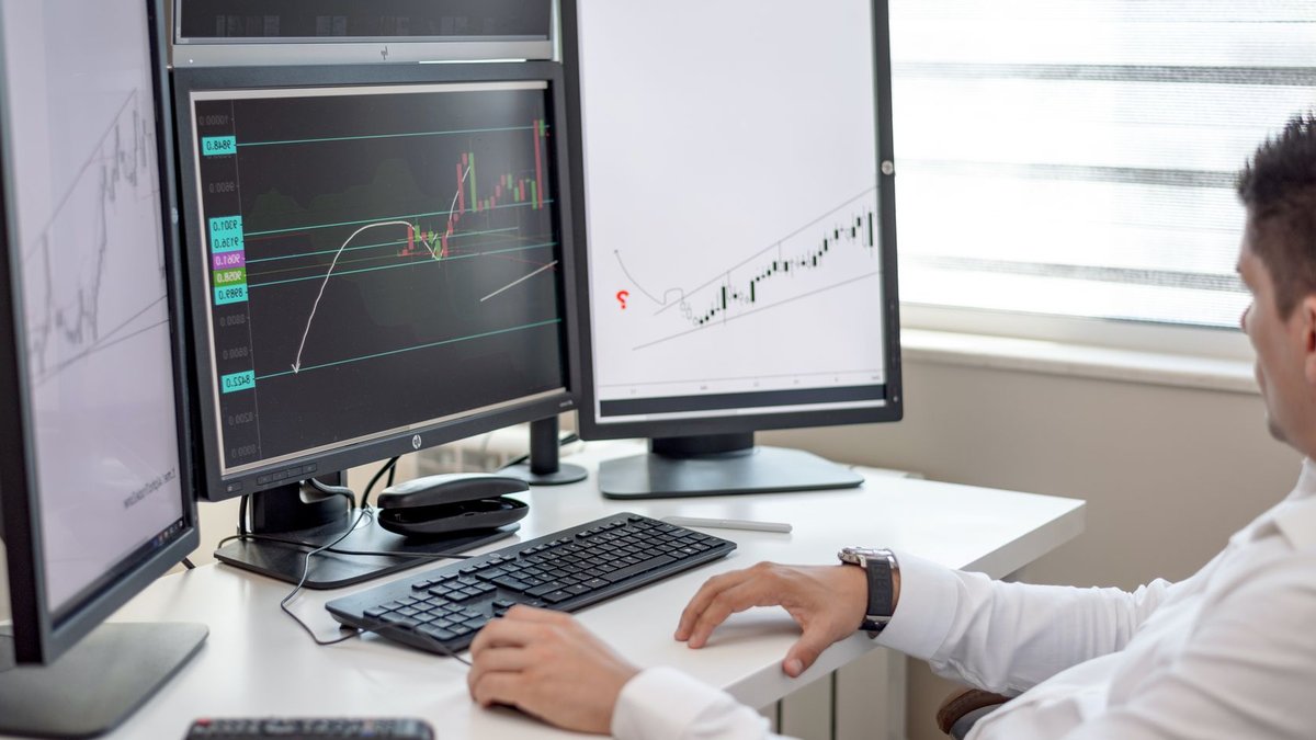 A businessman at his desk analyzing financial charts on multiple monitors.