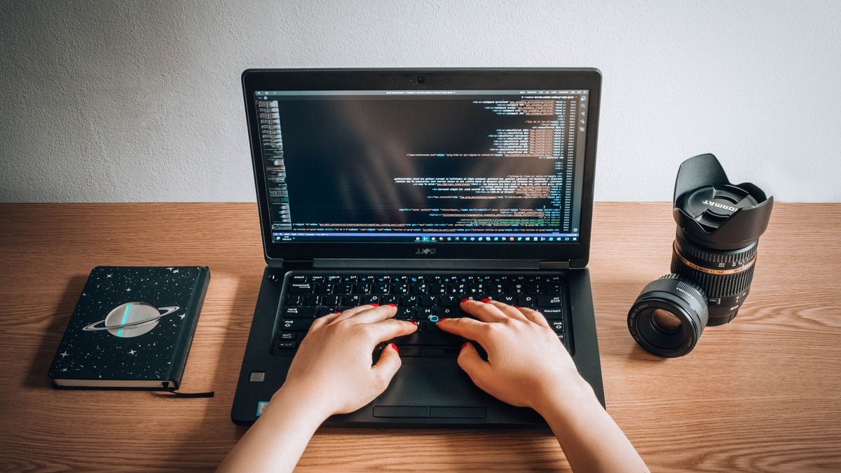 Microsoft AI simplifies interactive data chart creation A woman coding on a laptop with a camera lens and notebook on a wooden desk in a home office.