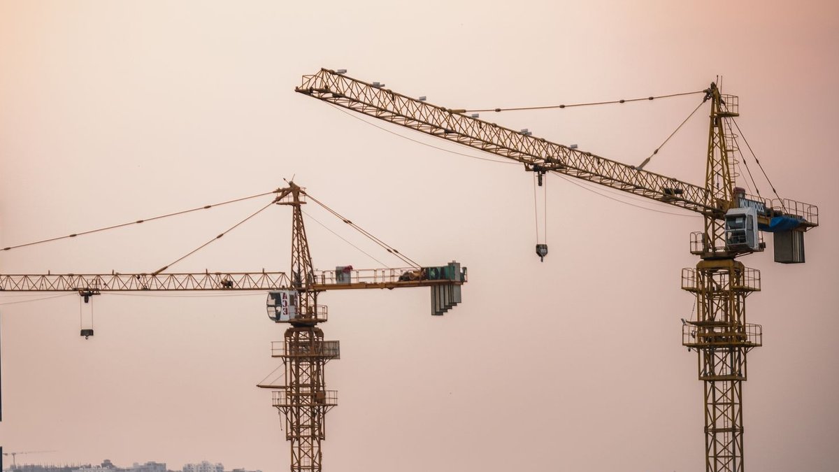 Skyline view of an urban construction site with prominent tower cranes at dusk.