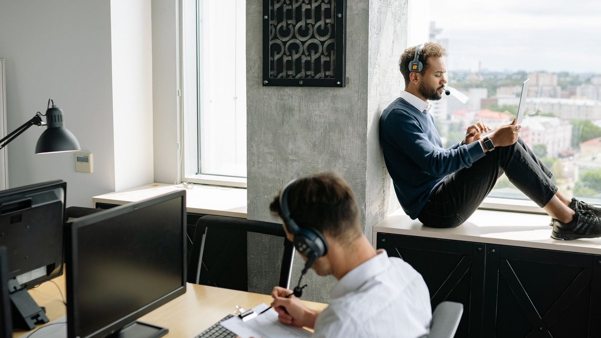 Banks Cut Underperforming AI Agents Two call center agents working in a modern office, one seated at a computer and another using a tablet by the window.