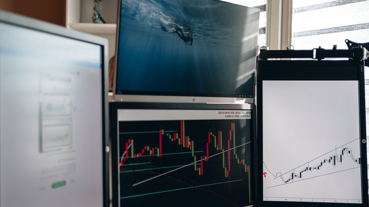 Plus500 upgrades 2026 profit outlook after strong quarterly gains A home office setup featuring multiple monitors displaying trading charts and data analysis.