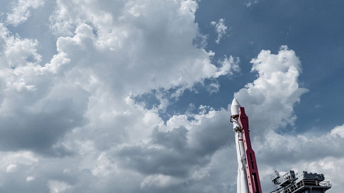 A shot across an expanse of low forest of a rocket launching into blue skies.
