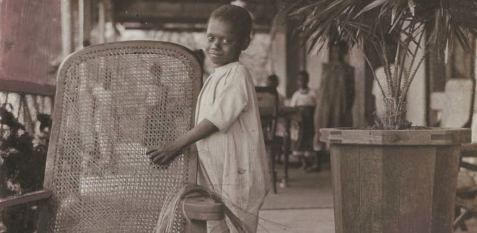 Een vrijgekochte slaaf bezig met stoelenmatten op de voorgalerij van de zendingswoning&rsquo;