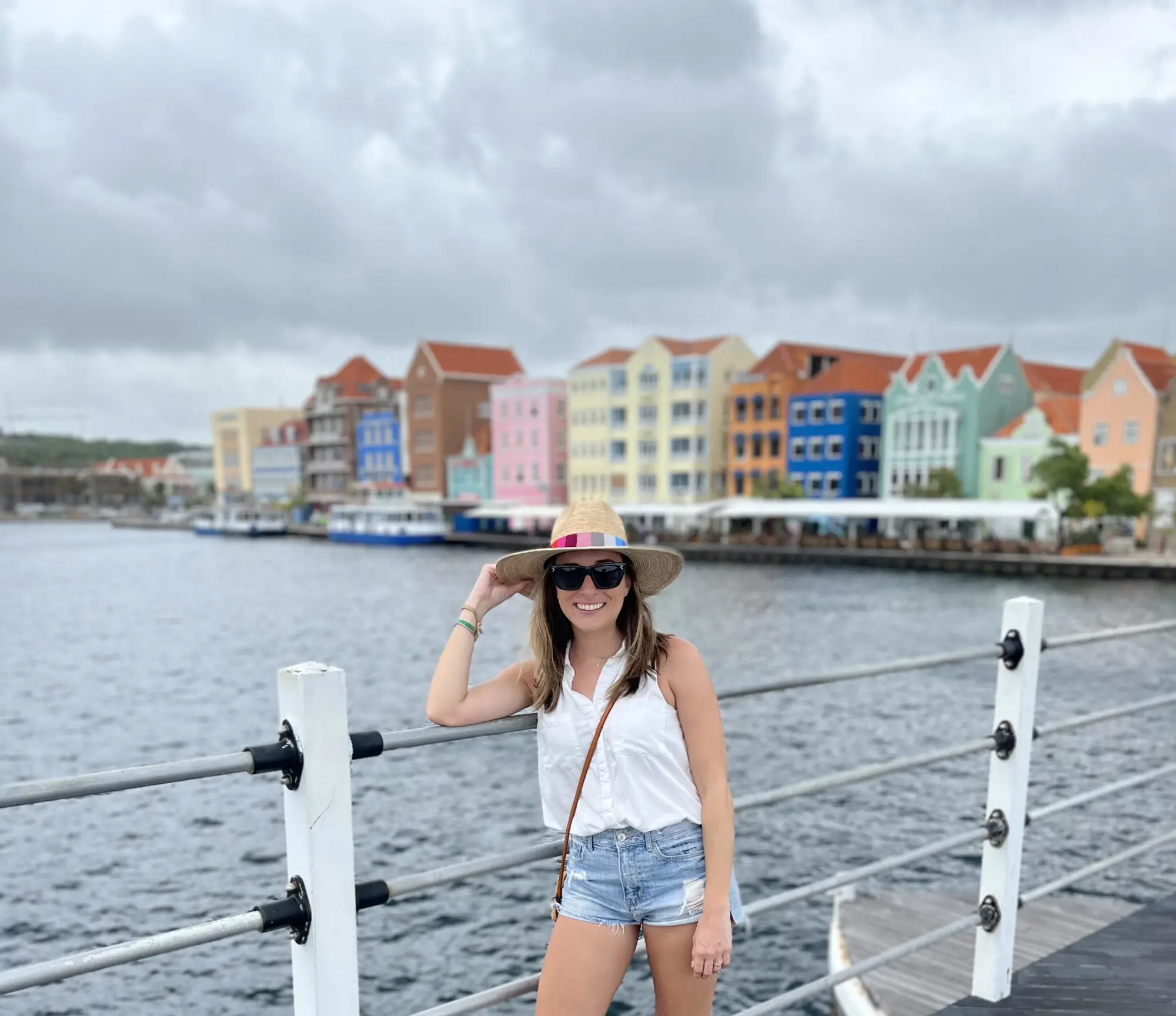 A woman standing in front of waterbody with colorful buildings in the distance.