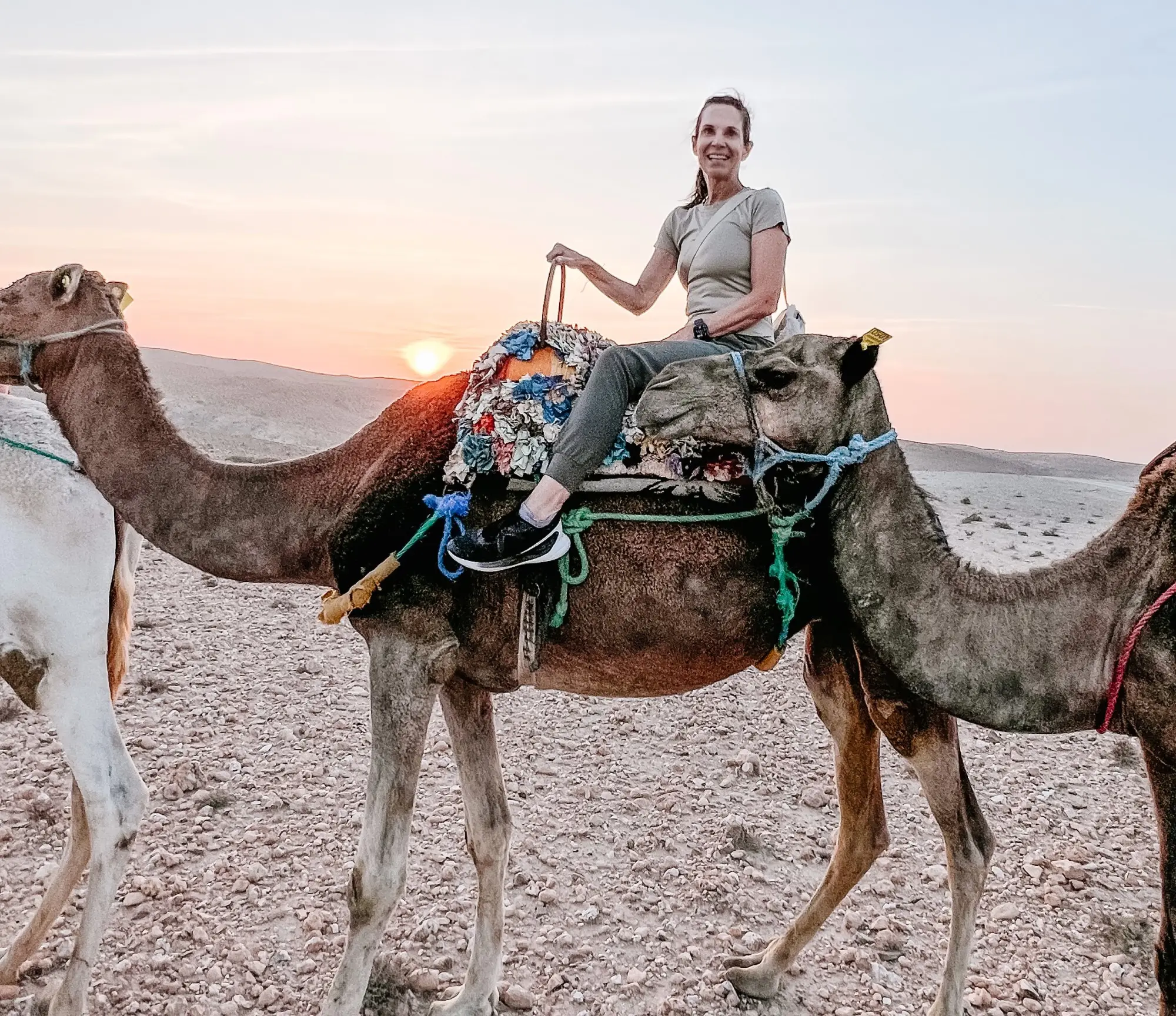 A lady sitting on a camel during sunset.