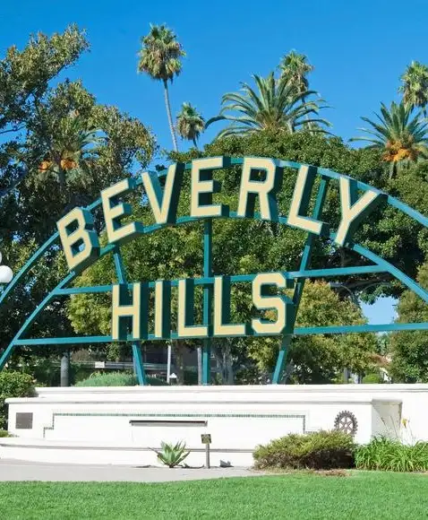 Beverly Hills signage at Beverly Gardens Park with palm trees and a clear sky in the distance.
