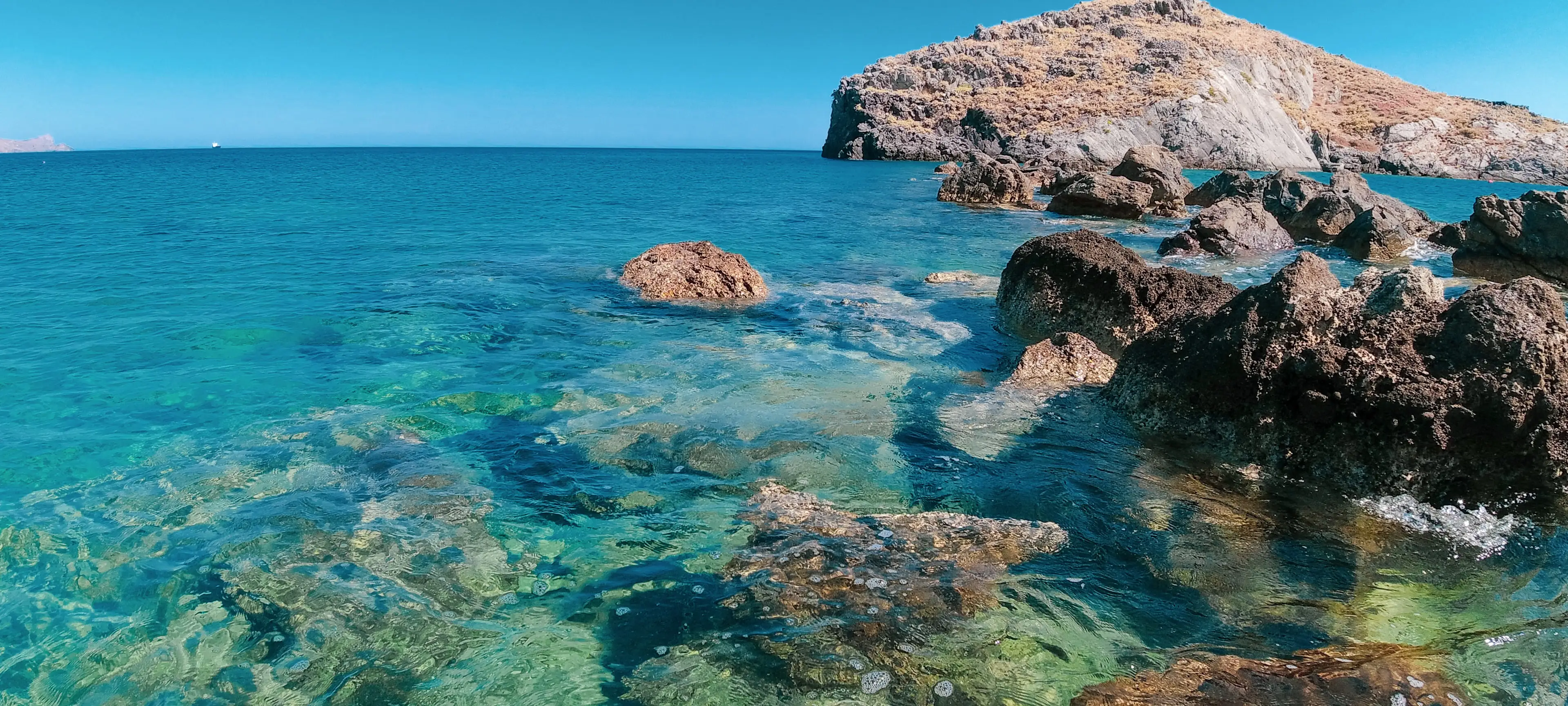 blue clear water with tan rocks and blue sky in Crete