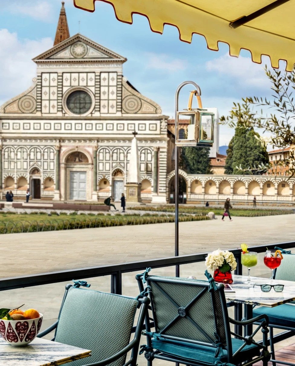 The terrace at the Place Firenze with blue patio chairs and a yellow awning, overlooking the Santa Maria Novella Basilica across the piazza.