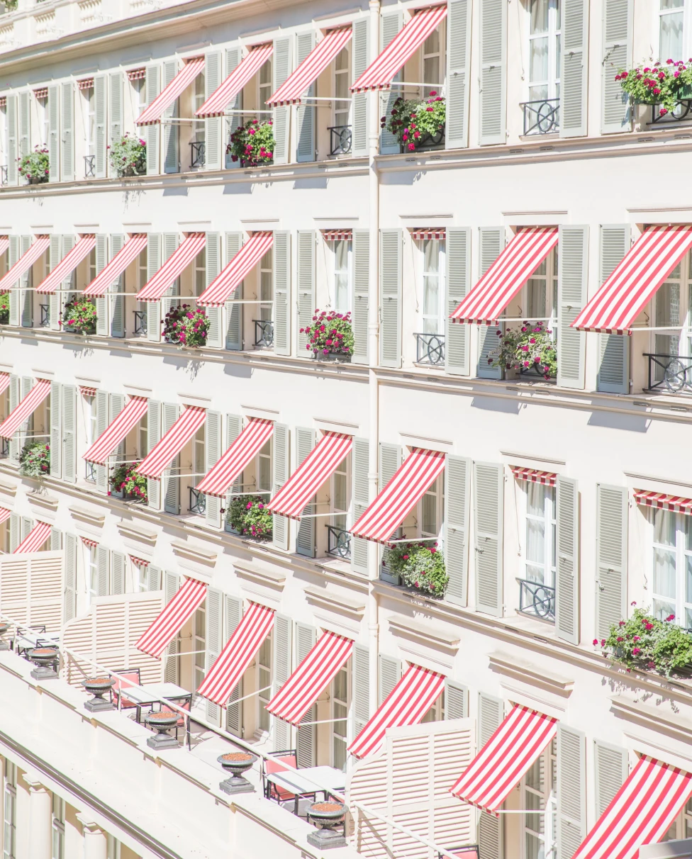 French building with red-and-white awnings over flower-decorated balconies