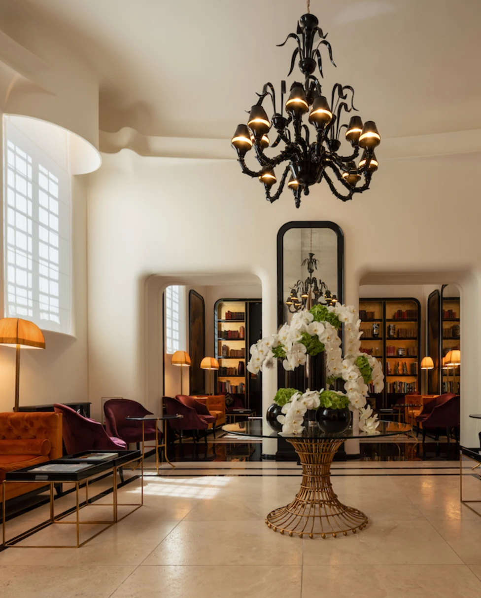 The foyer at the Palazzo Ripetta, with orange couches, gold paintings, a large floral centerpiece and a black chandelier.