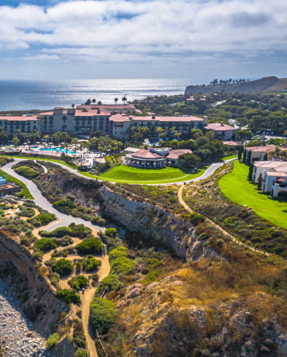 An aerial view of Terranea Resort on the coast with vast green areas and pools, surrounded by ocean and greenery.