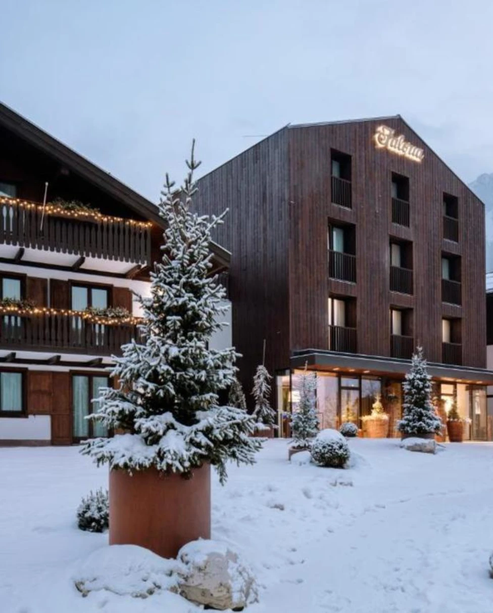 The exterior of the wooden Faloria Mountain Spa Resort on a snowy day, with green trees and mountains surrounding it.