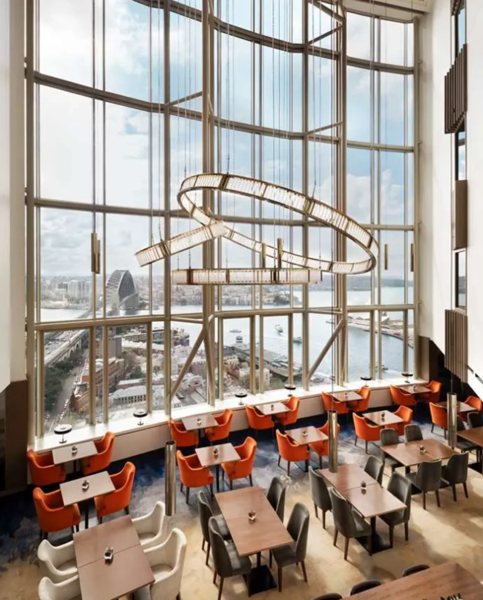 The restaurant at the Shangri-La Sydney, with tables underneath a tall ceiling and architectural chandelier with views of Sydney out the floor-to-ceiling windows.