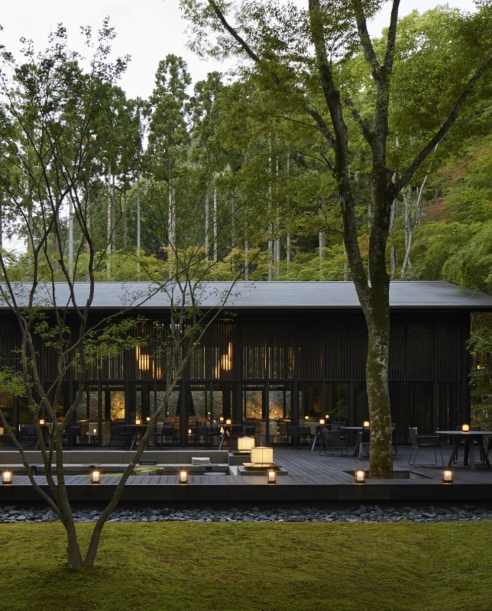 The exterior of the Aman Kyoto hotel, a black-single story building with lanterns and trees surrounding it.