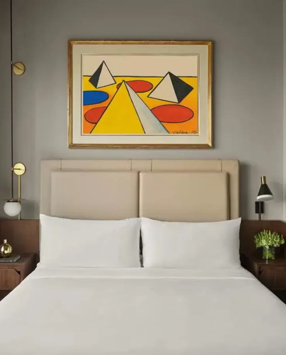 a modern, geometric painting over a white hotel bed