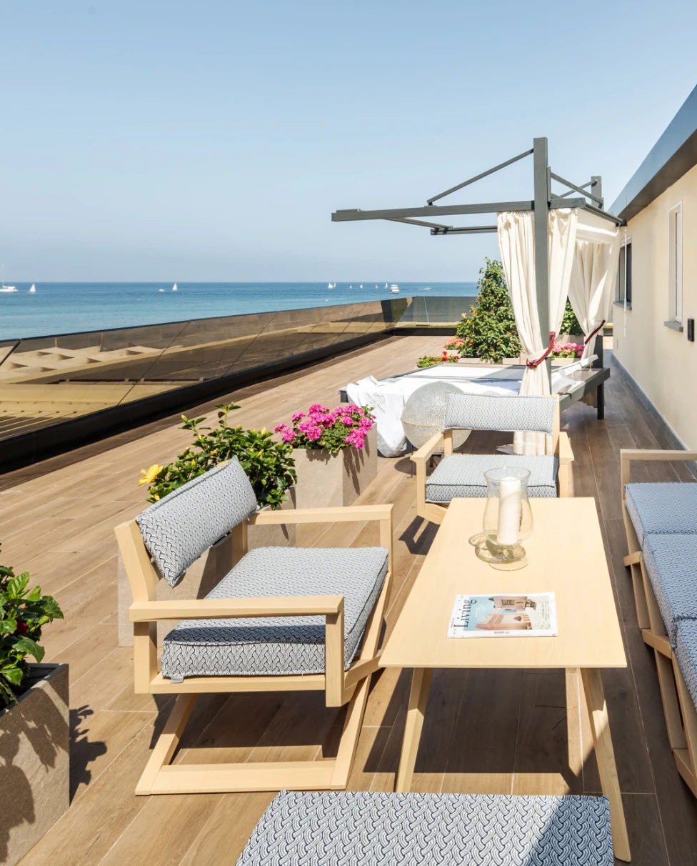 Outdoor terrace with flowers and seating area over looking ocean with sail boats