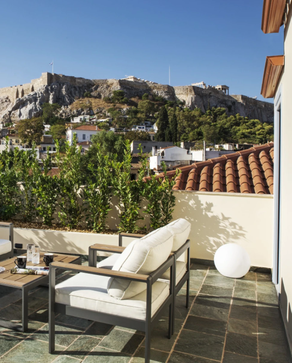 A view of the relaxed rooftop terrace at A77 suites with two double seats and a table and a view of ancient ruins in Athens.