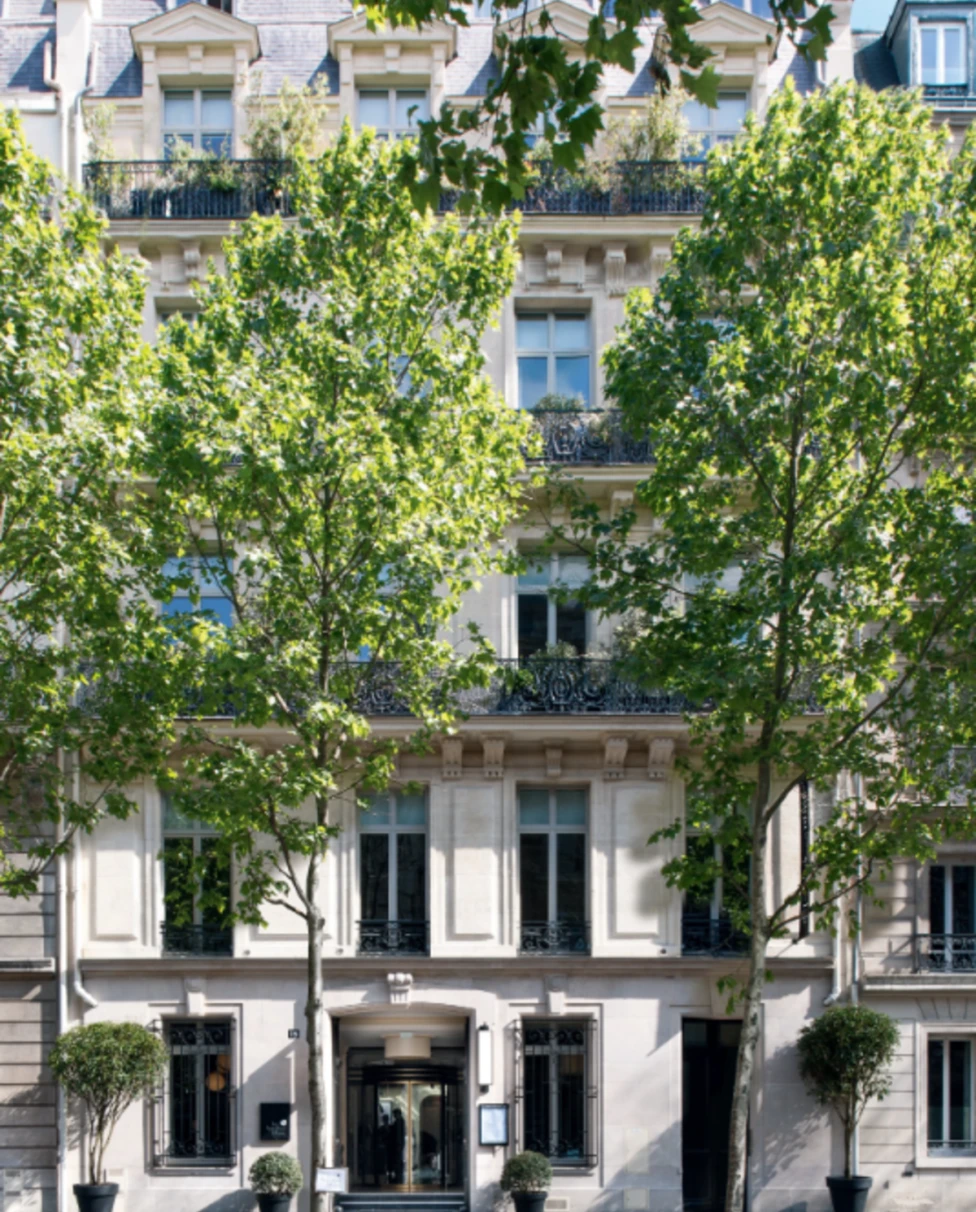 The facade of Le Narcisse Blanc Hôtel & Spa with tall trees on the sidewalk.