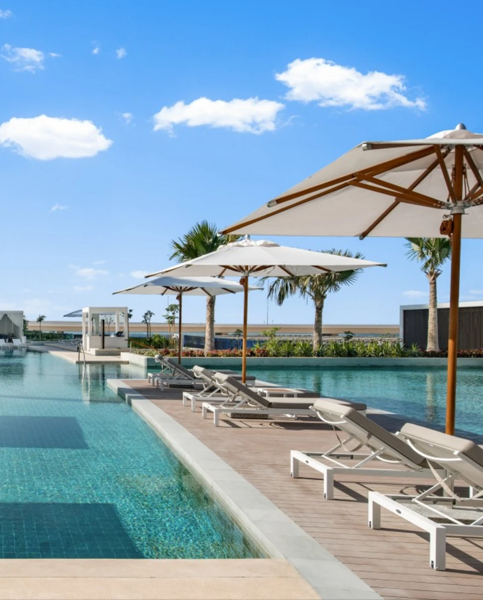 infinity pool surrounded by white loungers, cabanas, and palm trees