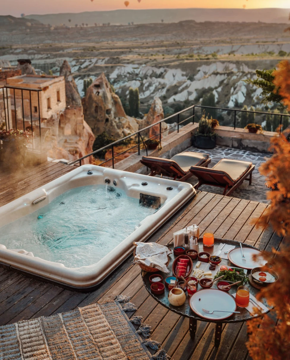 A view from above of a deck with a hot tub at sunset with hot air balloons flying in the distance.